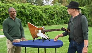 Two men looking at guitar on Antiques Roadshow outdoor set