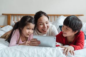 kids sitting on bed with mom holding a tablet