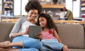 mom and daughter sitting on couch together looking at tablet